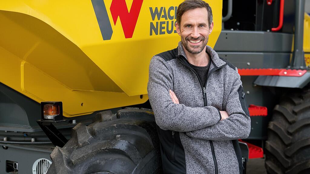 WN_global_image_service_06.jpg Wacker Neuson customer standing and smiling with arms folded in front of a Wacker Neuson wheel dumper.
