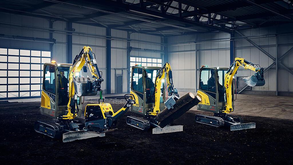 three yellow mini excavators in industry hall carrying heavy equipment