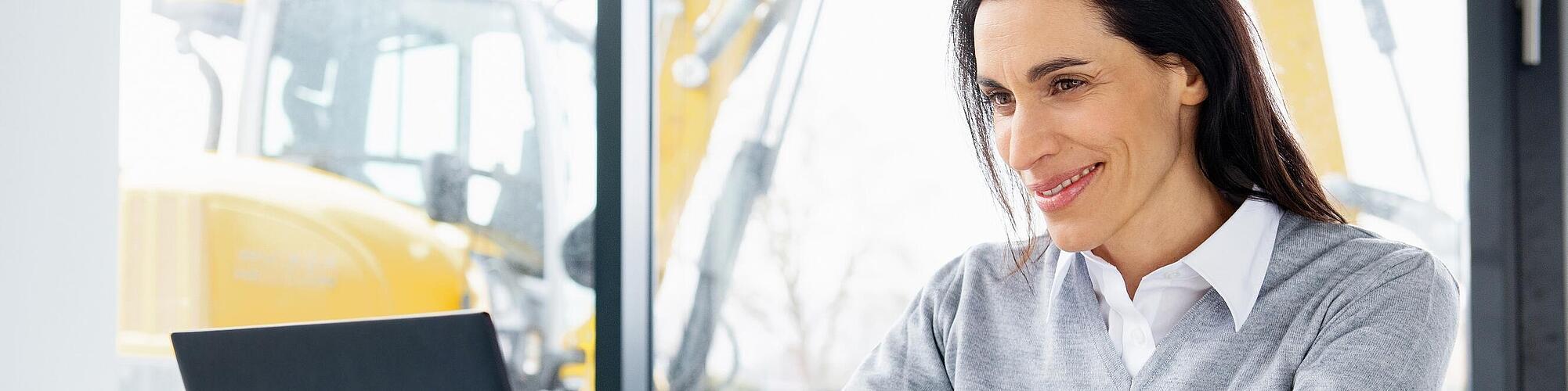 Il dipendente Wacker Neuson sta seduto davanti al portatile e sorride.