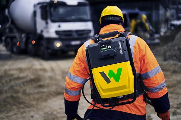 Il lavoratore edile trasporta lo zaino  convertitore batteria ACBe di Wacker Neuson in un cantiere edile.