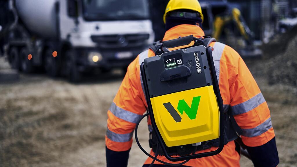 Il lavoratore edile trasporta lo zaino  convertitore batteria ACBe di Wacker Neuson in un cantiere edile.