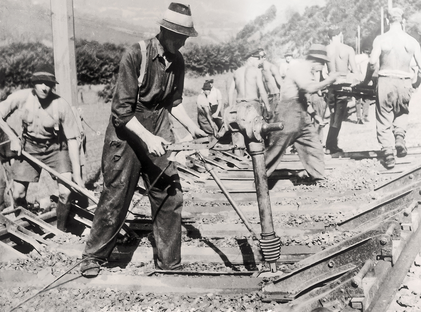 Operai ferroviari d'epoca che utilizzano un costipatore manuale per la compattazione del terreno sotto i binari in un cantiere